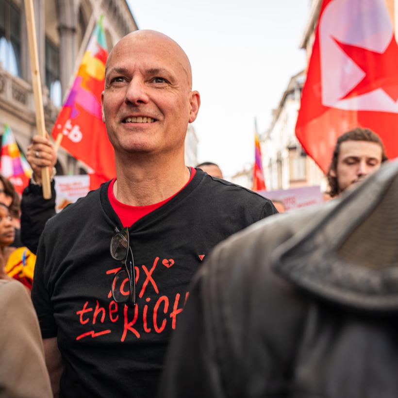 Een man midden in een betoging met een T-shirt met de tekst ‘Tax The Rich’.