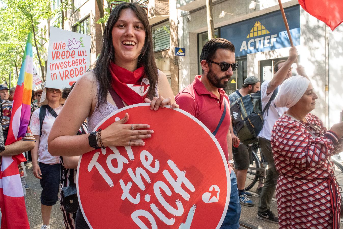 1 mei in Antwerpen, een jonge vrouw draagt een bord met ‘Tax the rich’