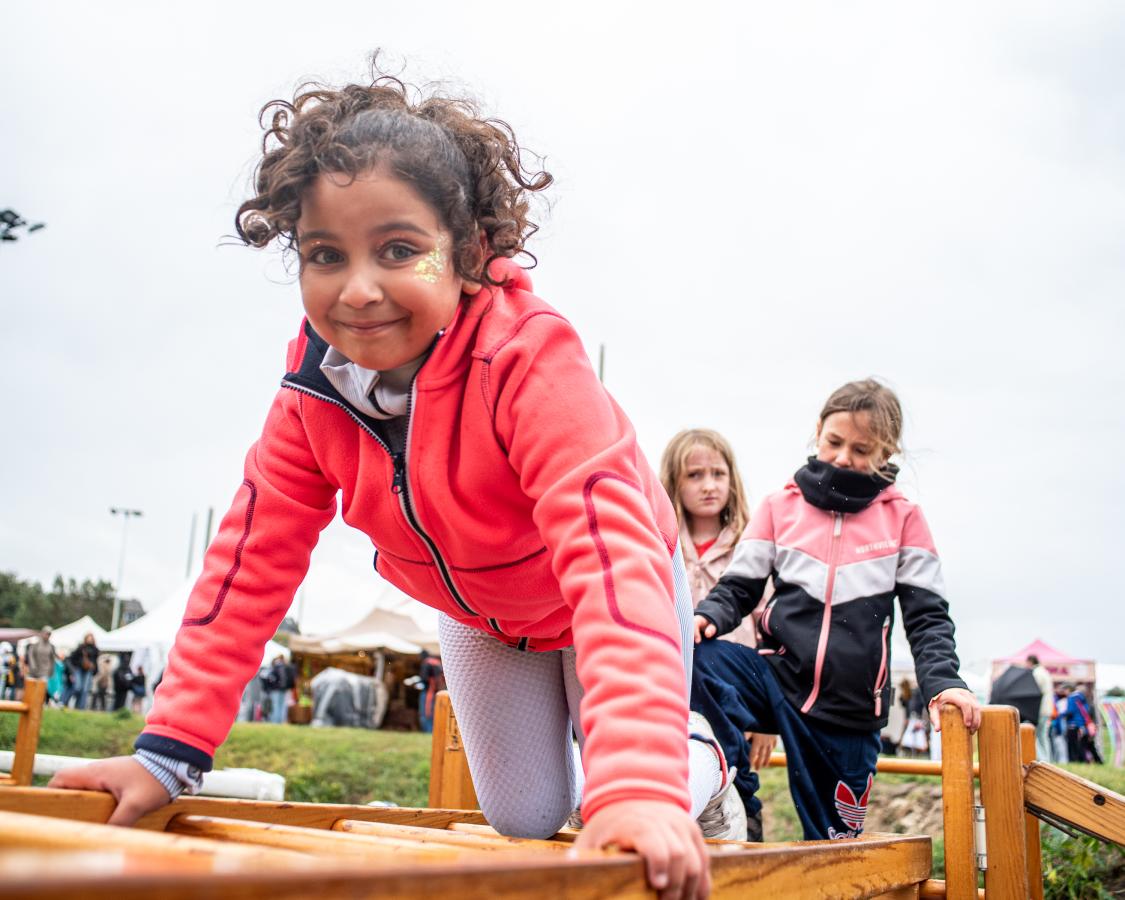 Een jong kind met krullen klimt op een houtstructuur
