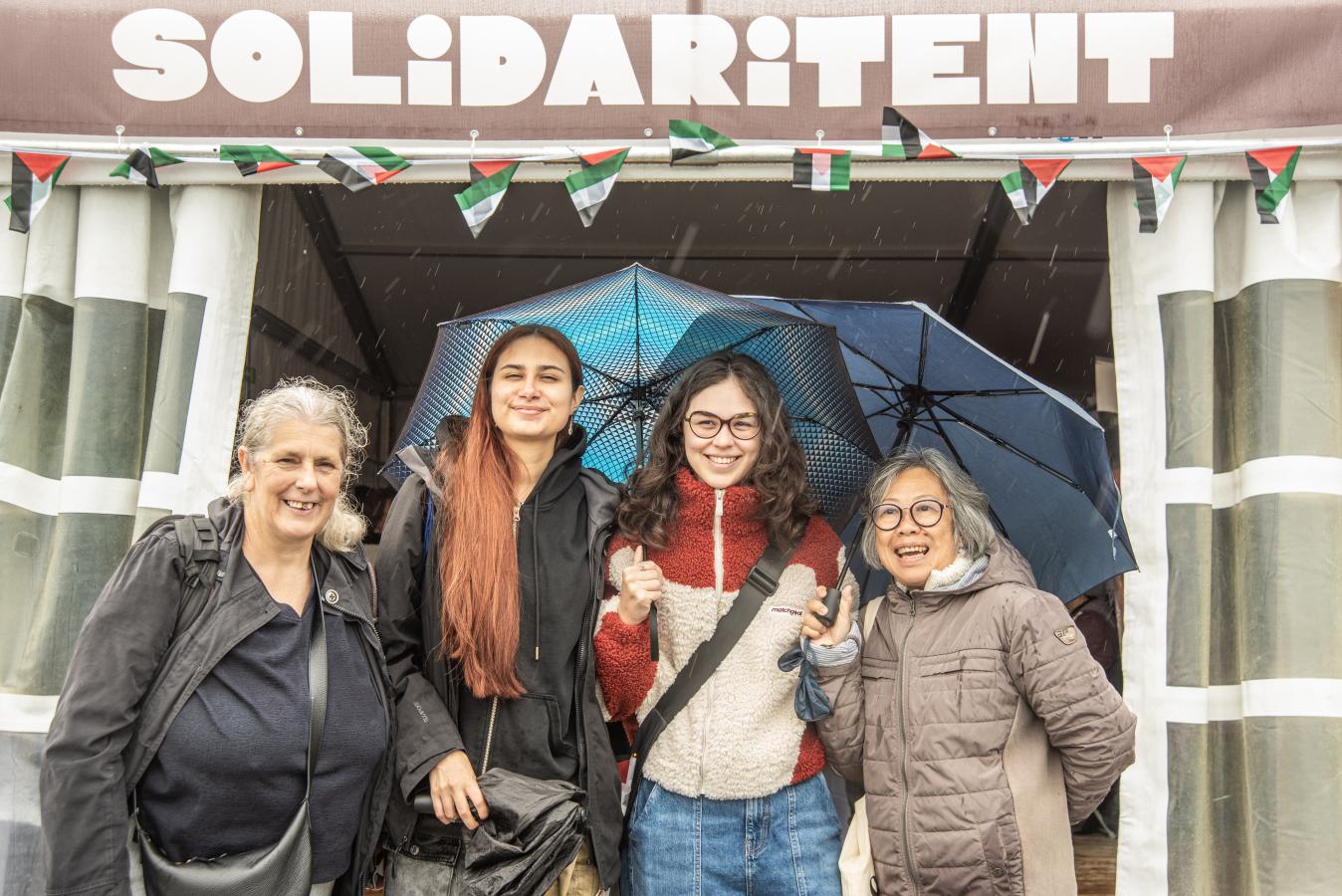 Een groep jonge en oude mensen staan voor de solidaritent met paraplu's