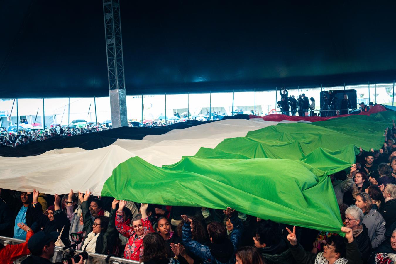 Een grote palestijnse vlag wordt over een grote massa mensen getrokken