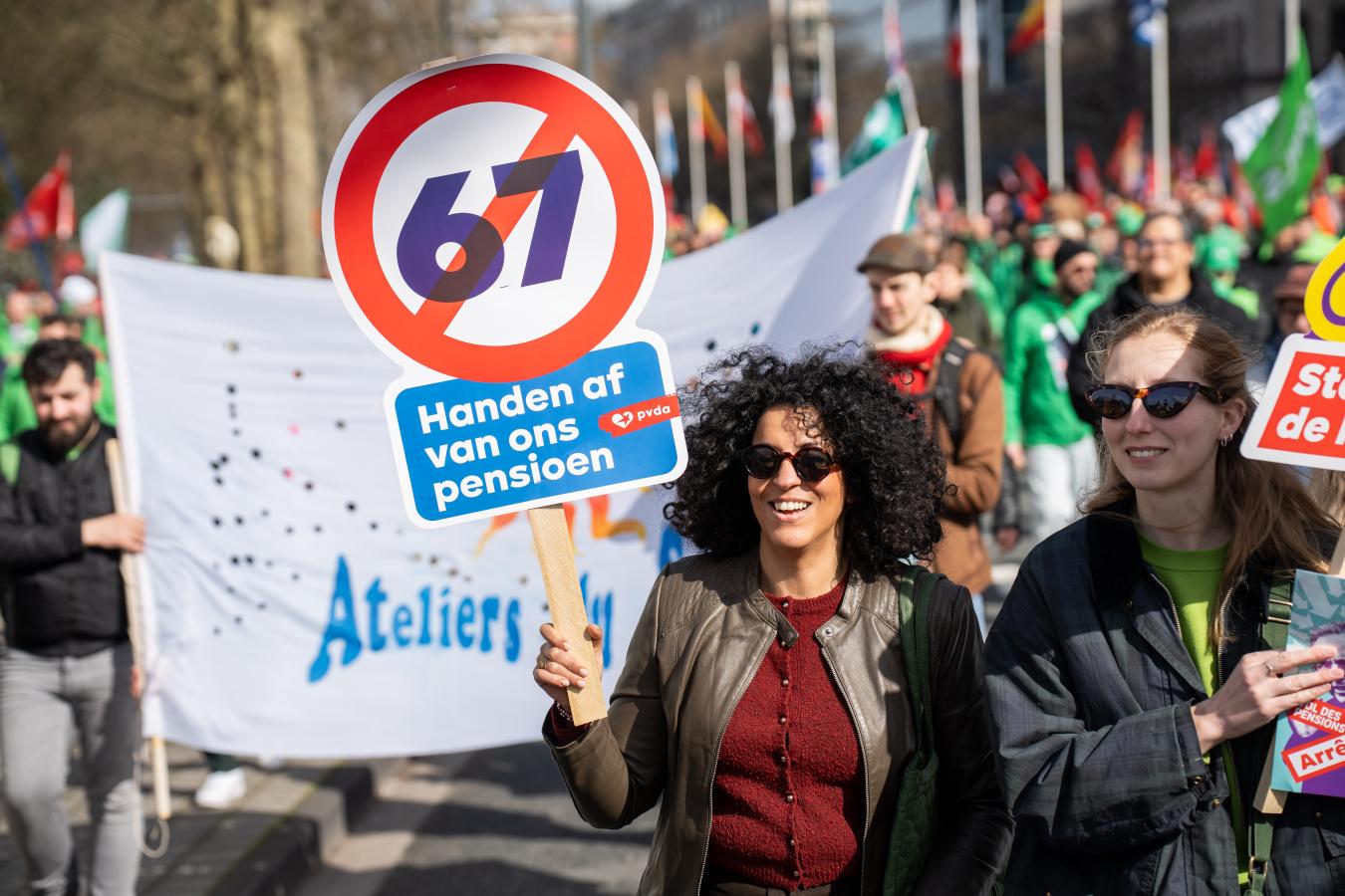 beeld 1: lachende vrouw tijdens de nationale betoging van 12 maart, met een bordje: 'handen af van ons pensioen’