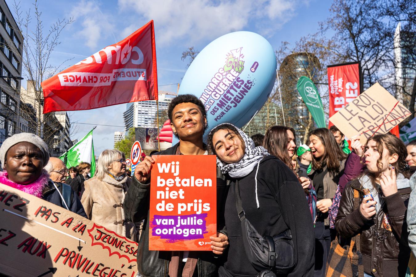 beeld 3: twee jongeren met een bordje 'Wij betalen niet de prijs van jullie oorlogen', tijdens de nationale betoging van 12 maart