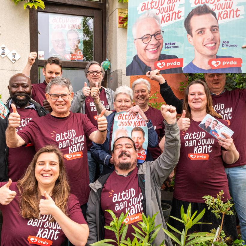 Leden van een PVDA-basisgroep dragen T-shirts met 'Altijd aan jouw kant' op en poseren voor een verkiezingsaffiche van Peter Mertens en Jos D’Haese