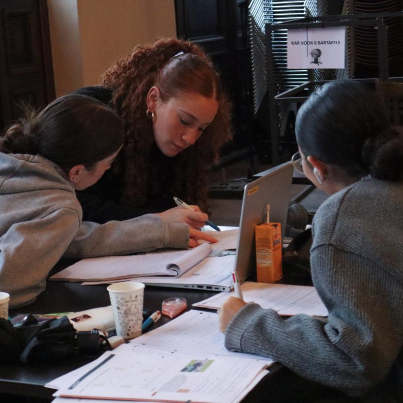 Een vrijwilliger helpt twee jongeren met studeren tijdens de Boostdays van RedFox