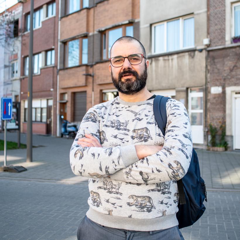 Een jonge man poseert in een straat, met gekruiste armen