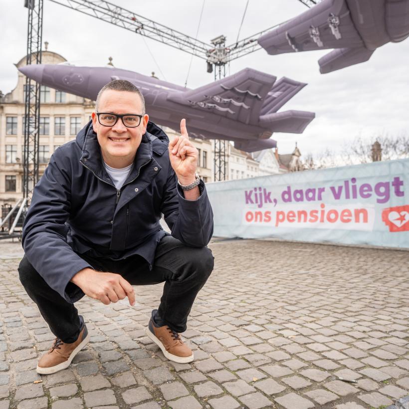 Raoul Hedebouw gehurkt voor de 3 opblaasbare F-35's en het spandoek 'Kijk, daar vliegt ons pensioen’