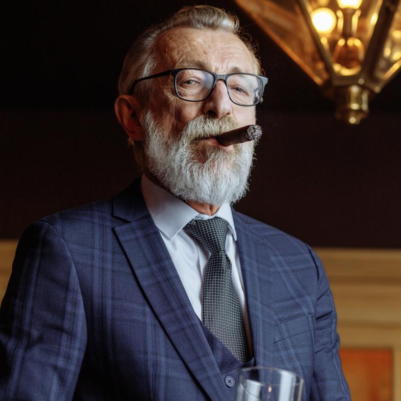 Een miljonair met een sigaar en een glas alcohol kijkt neer op de camera.