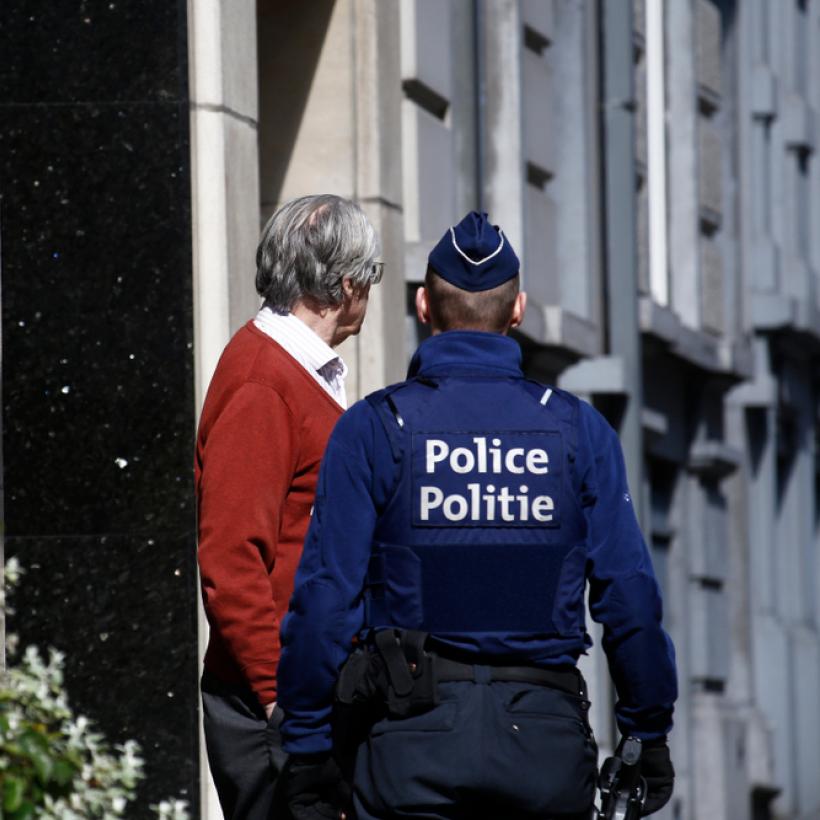 Een Belgische politieagent spreekt met een man voor de ingang van een huis.