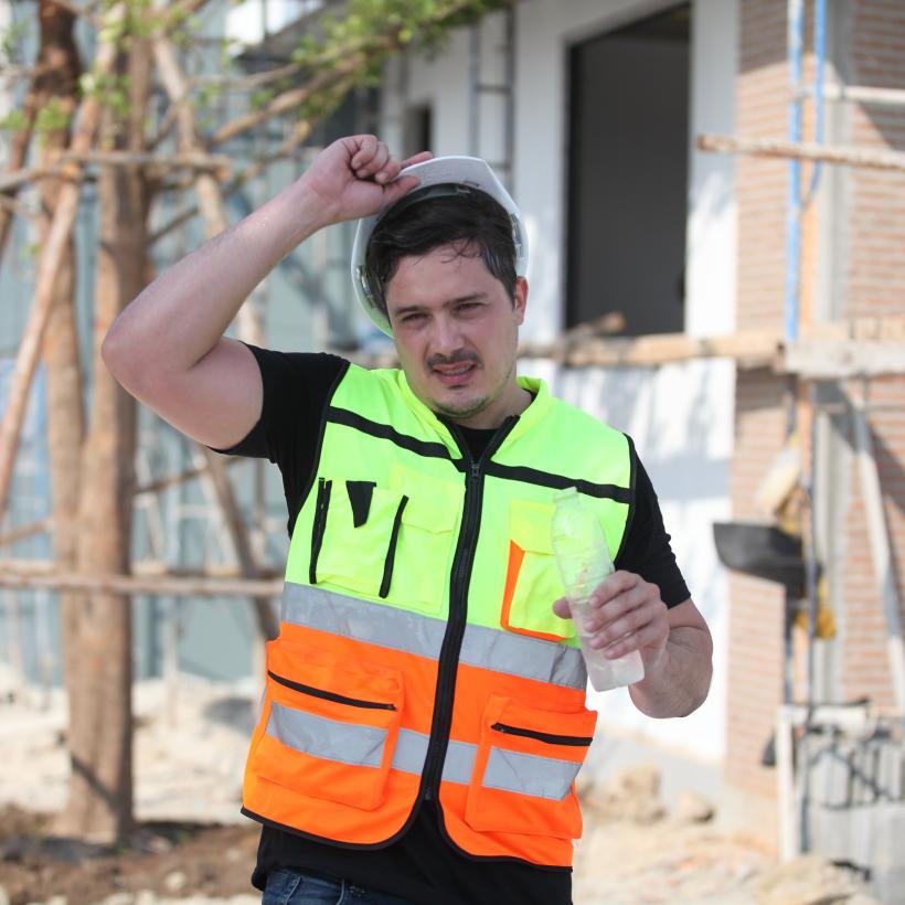 Een bouwvakker die in de hitte aan het werk is, met een fles water in de hand 