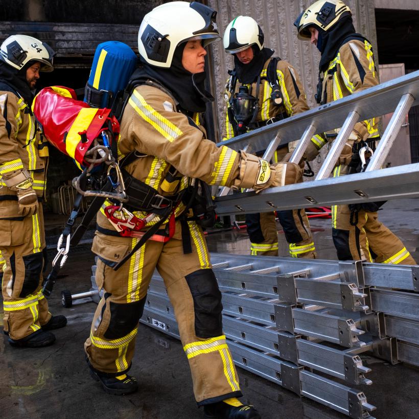 Een groep brandweerlieden draagt een ladder tijdens een interventie