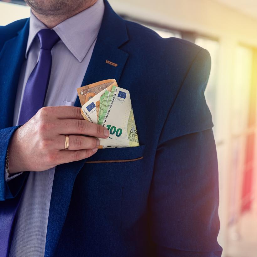 Een man in maatpak stopt een bundeltje bankbiljetten in zijn zak