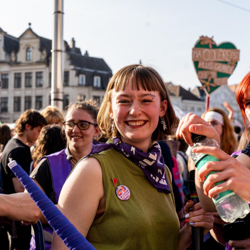 Een jonge vrouw glimlacht naar de camera te midden van de menigte tijdens een demonstratie voor vrouwenrechten