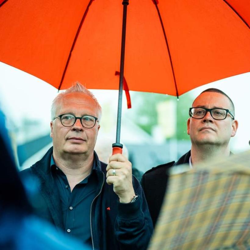 Peter Mertens en Raoul Hedebouw onder een paraplu tijdens een 8 mei-viering