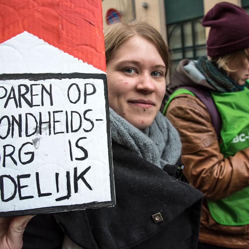 vrouw houdt een groot sigarettenpakje vast met de slogan 'besparen op gezondheidszorg is dodelijk'