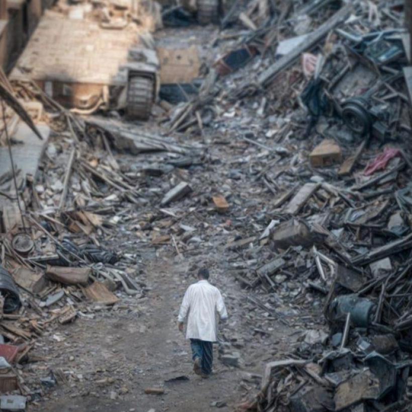 Beeld van dokter Hussam Abu Safiya die stapt tussen het puin van vernielde gebouwen, met op de achtergrond een Israëlische tank