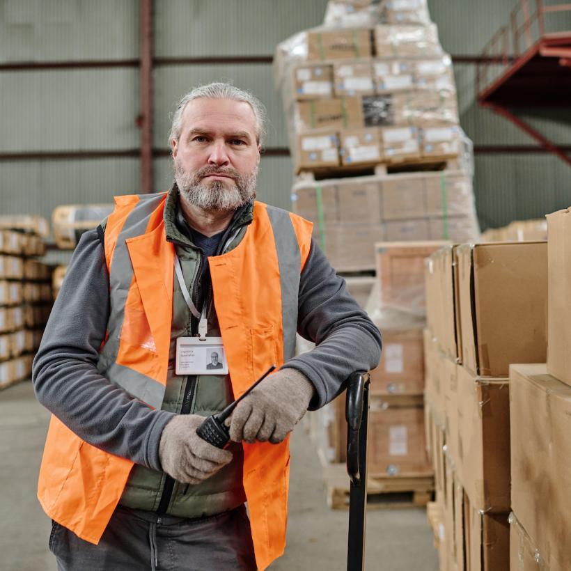 beeld van een arbeider in een magazijn, die in de camera kijkt