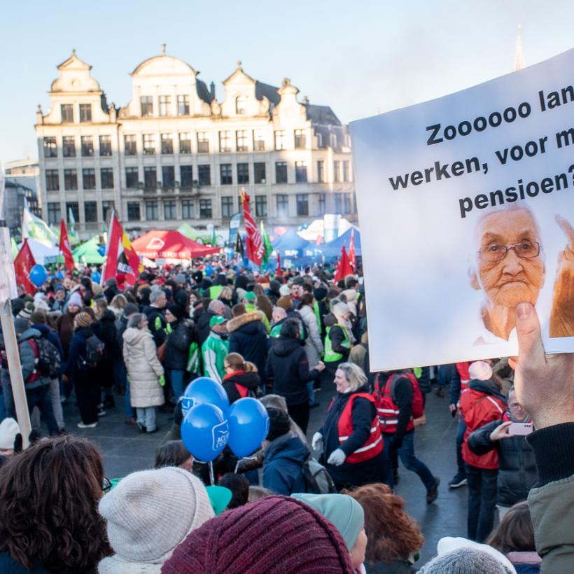 Beeld van menigte op een betoging, met een zichtbare slogan: “Zooooo lang werken voor minder pensioen?”