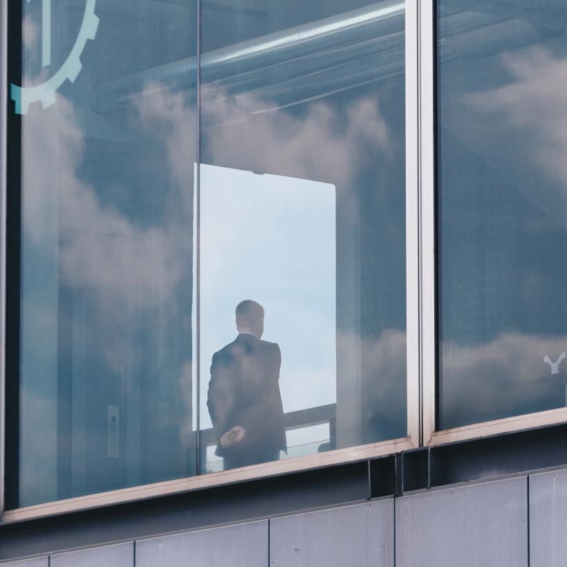 Un homme d'affaire de dos derrière la vitre d'un immeuble.