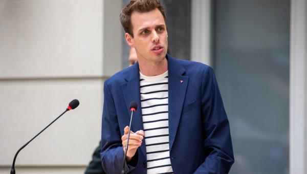 Jos D'Haese in het Vlaams parlement. Hij draagt een blauwe blazer en een shirt met diagonale dunne strepen. Hij spreekt in de micro. Zijn gezichtsuitdrukking is ontevreden.