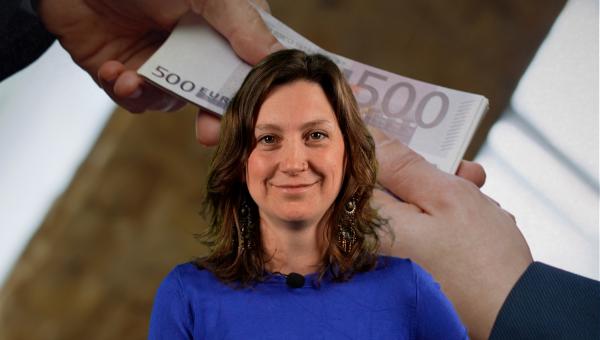 Line De Witte kijkt in de camera. Op de achtergrond wisselen twee mensen geldbriefjes uit.